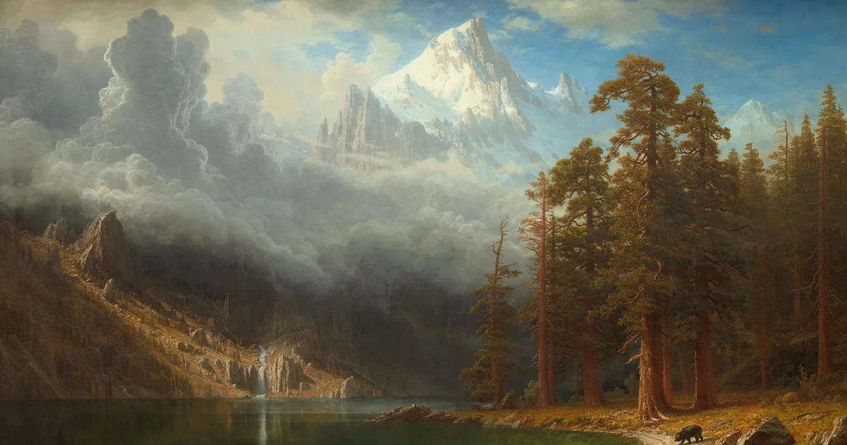A snow-capped peak rising out of the clouds above a lake lined with sequoias